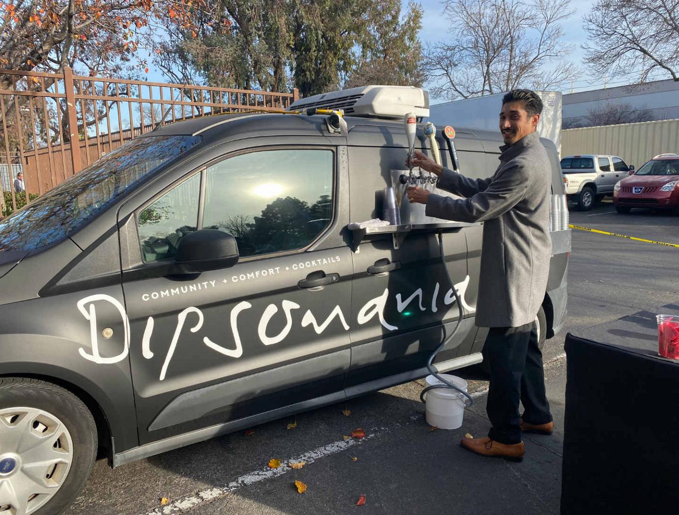 Outdoors, a male pouring beer from Dipsomania's van drink dispenser